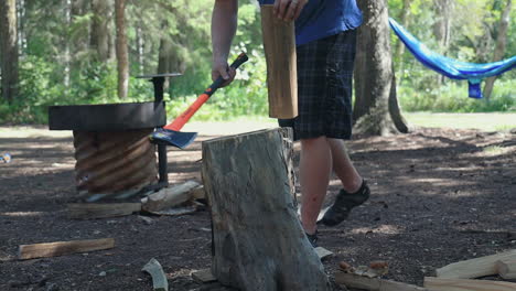 Man-in-t-shirt-and-shorts-splits-firewood-with-axe-while-camping