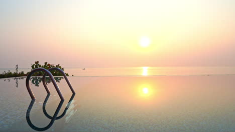 Sonne,-Die-Sich-Bei-Sonnenuntergang-über-Infinity-Pool-Wasser-Mit-Meer-Im-Hintergrund-Widerspiegelt