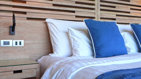Hotel-room-interior-with-king's-size-made-up-bed,-white-and-blue-pillow-and-wooden-headboard-daytime