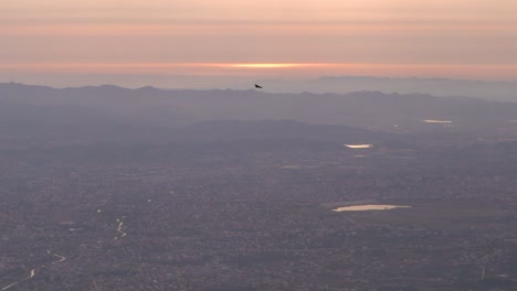 Adlersilhouette,-Die-Bei-Sonnenuntergang-über-Ein-Wunderschönes-Weites-Stadtpanorama-Fliegt
