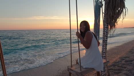 Young-and-carefree-girl,-looking-and-smiling-at-camera-while-swinging-next-to-ocean