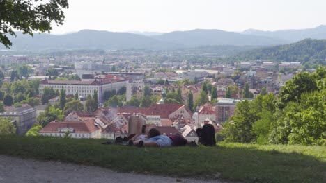 Una-Pareja-Descansando-En-El-Césped-Con-Una-Vista-Panorámica-De-Ljubljana-En-Eslovenia