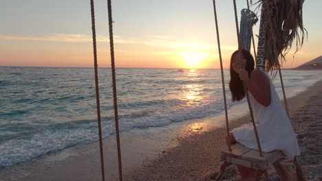 Young-girl-on-swing-next-to-beautiful-ocean-at-sunset