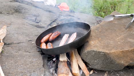 A-close-up-shot-of-sausages-and-bacon-being-cooked-in-a-pan-over-a-camp-fire-in-rural-Africa