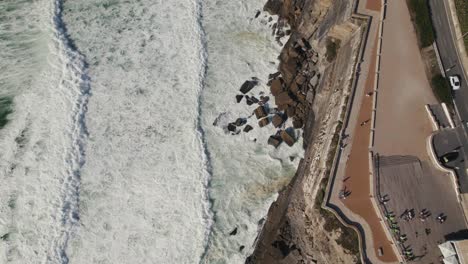 Cinematic-aerial-top-down-dolly-in-shot-of-foamy-waves-hitting-coastal-rocky-cliffs