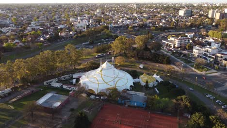 Ariel-view-of-Anima-circus-white-tent-in-Sarmiento-Park-in-Buenos-Aires,-Argentina-and-in-the-background-a-beautiful-view-of-the-city