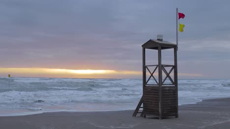 Die-Sonne-Scheint-Durch-Die-Wolken-An-Einem-Leeren-Strand-Mit-Rettungsschwimmerturm-Bei-Sonnenuntergang