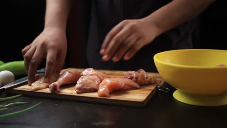Transferring-chicken-pieces-to-a-yellow-bowl-from-a-wooden-chopping-board-by-hands