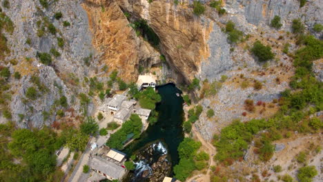 Drone-View-Of-Blagaj-With-Tekija-On-The-Base-Cliffs-Along-Buna-River-In-Bosnia-and-Herzegovina