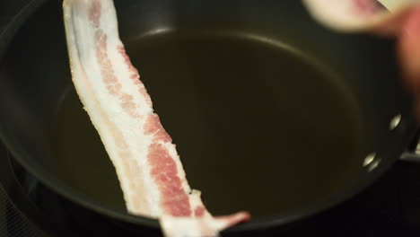 Placing-slices-of-bacon-inside-a-pan-to-fry