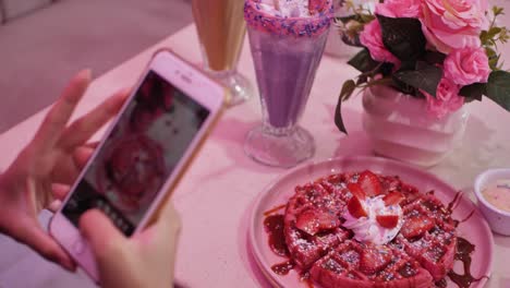Beautiful-woman-taking-several-photos-of-her-colorful-waffle-and-taro-frappe-for-Instagram-in-a-pink-themed-coffee-shop