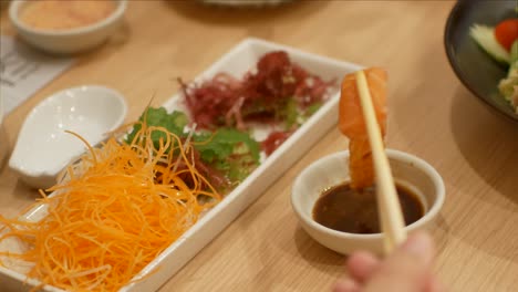 4k-video-of-using-chopctick-pick-slamon-sashimi-dipping-into-soy-sauce,-raw-fish-Japanese-style-food