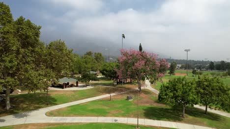 Bright-sunny-Pasadena-public-recreational-park-aerial-view-rising-to-misty-mountain-skyline-in-distance