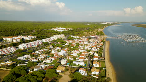 Aerial-bird's-eye-view-over-Puerto-Marina-El-Rompido---private-real-estate-houses,-beachline,-dock-with-boats-and-yachts-on-Piedras-river,-hotels-surrounded-with-Cartaya-Stone-Pine-Forest