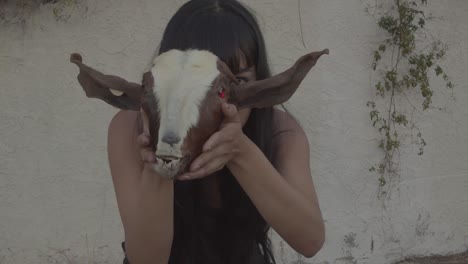 A-young-woman-holding-a-goat-head-prop-with-red-eyes