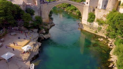 Aerial-View-Of-People-At-Stari-Most-Over-Neretva-River-With-Koski-Mehmed-Pasha-Mosque-In-Background-In-Mostar,-Bosnia-And-Herzegovina