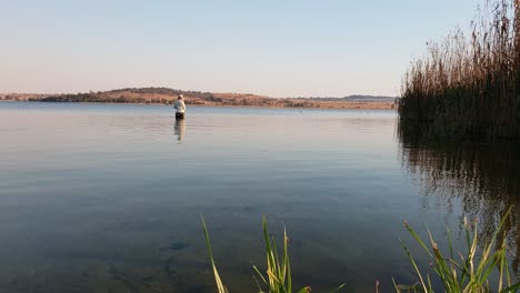 Una-Chica-Pescando-Lubina-Mientras-Vadea-Dentro-De-Un-Lago-En-Un-Día-Tranquilo-Y-Soleado