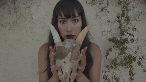 Zoom-in-of-beautiful-woman-unveiling-her-face-behind-the-skull-of-an-animal-with-horns