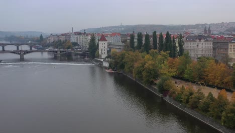 Aerial-cinematic-view-of-Prague,-Czech-Republic,-Prague-cityscape-showing-medieval-bridges-and-boats-on-the-Vltava-river-in-autumn
