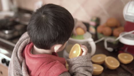 Niño-Asiático-Sosteniendo-Naranjas-Y-Haciendo-Jugo-Con-Un-Exprimidor-Eléctrico