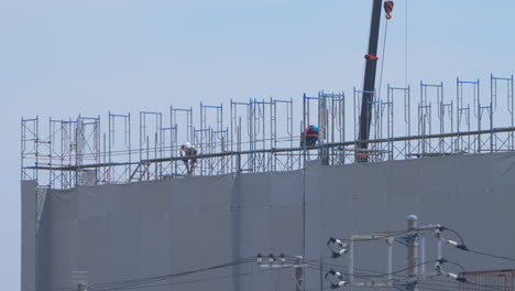 Trabajadores-De-La-Construcción-Que-Trabajan-En-Andamios-En-Un-Proyecto-De-Construcción-Con-Grúa-En-Un-Clima-Cálido