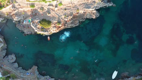 Bird's-eye-view-people-jumping-off-the-cliff-into-water,-Avlemonas-Greece