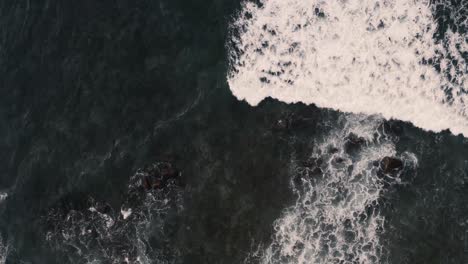 Atemberaubende-Luftaufnahme-Des-Dunkelblauen-Ozeans-Und-Der-Riesigen-Wellen,-Die-Mit-Plätscherndem-Und-Weißem-Schaum-Auf-Felsklippen-Krachen