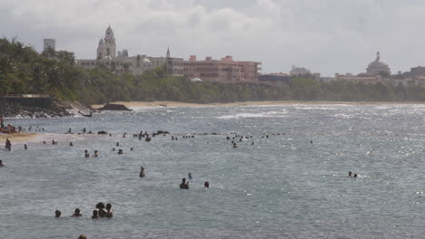 People-swimming-in-the-sea-with-city-background-in-San-Juan,-Puerto-Rico