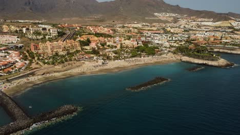 Amazing-Drone-Shot-of-Seashore-Seaside-Of-City-With-Buildings-With-Mountains-In-The-Background-Blue-Water-Sea-Drone-Shot-Palm-Tree-Panoramic-View-In-Spain-Tenerife-Los-Cristianos