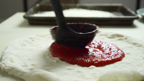 Close-up-of-Chef-while-spreading-Tomato-Sauce-on-Pizza-Dough-with-a-Ladle-in-Traditional-Italian-Pizza's-Restaurant