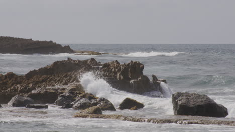 Waves-hitting-and-splashing-into-the-rocks-seaside-of-the-beach-on-a-cloudy-day