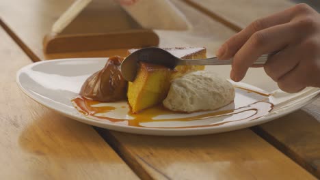 Hand-using-spoon-to-cut-delicious-flan-with-dulce-de-leche-and-cream
