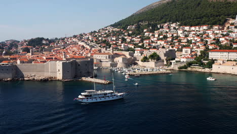 Landscape-With-Sailing-Ship-Outside-The-Harbor-In-The-Bay-Of-The-Walled-City-Of-Dubrovnik,-Croatia---aerial-drone-shot