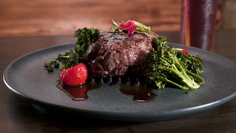 Perfectly-grilled-8-oz-prime-filet-mignon-on-a-bed-of-broccolini-with-stuffed-cherry-peppers-plated-on-black-rustic-stoneware-plate,-slider-HD