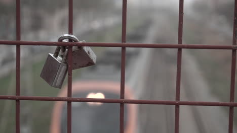 Two-love-locks-on-a-fence-of-a-bridge-over-train-tracks-as-a-train-passes-underneath