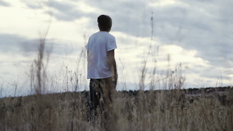 Slider-shot-through-tall-grass-of-young-man-staring-longingly-at-sunset