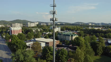 Aerial-rising-to-reveal-cell-phone-5G-communication-tower-in-busy-area,-4K
