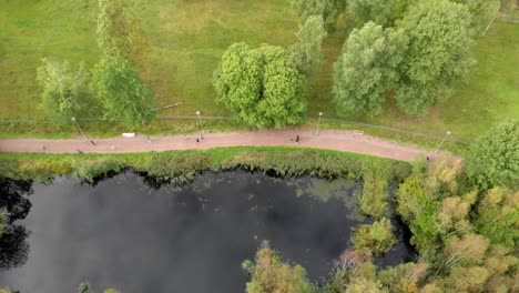 Unrecognizable-Kids-Running-and-Walking-by-a-Pond-in-the-Park,-Aerial