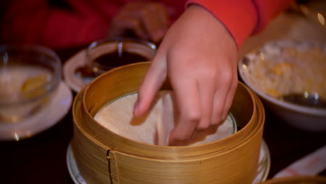 Girl-taking-a-pancake-wrap-from-a-bamboo-bowl-in-a-chinese-restaurant