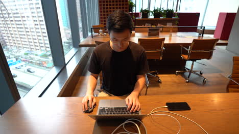 Chinese-Asian-millennial-with-glasses-working-on-laptop-in-empty-co-working-space-in-Hong-Kong