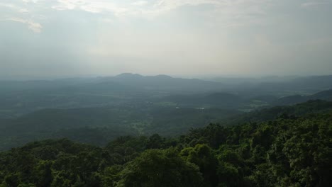 Mountains-and-hill-in-the-horizon-with-the-sun-setting,-a-lush-and-green-forest-in-the-foreground