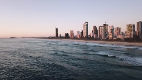 Drone-sunrise-aerial-shot-over-city-beach-of-stand-up-paddle-boarders-catching-waves