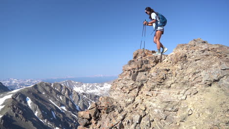 Montañero-Femenino-En-La-Cima-De-La-Cumbre-Rocosa-Caminando-Cuidadosamente-Con-Bastones-De-Trekking