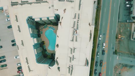 Drone-footage-of-an-apartment-complex-with-a-pool,-alongside-a-busy-road-with-traffic