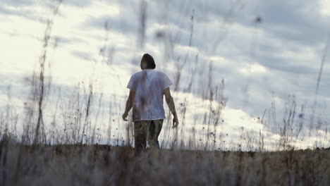 Man-walking-away-from-camera-towards-sunset-through-tall-grass,-slow-motion