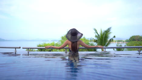 Back-of-the-woman-standing-near-infinity-pool-border-in-tropical-landscape-enjoying-view,-tranquil-beauty-in-nature