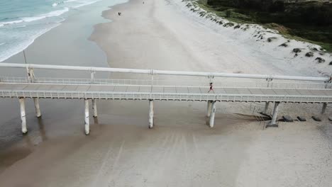 Drone-shot-of-female-running-on-beach-pier-in-summer-fitness-body--Gold-Coast-Queensland