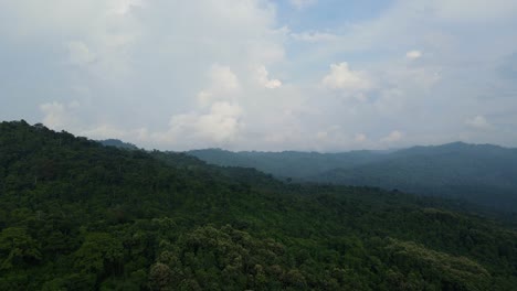 Aerial-footage-sliding-to-the-right-revealing-a-lush-rainforest,-mountains-in-the-horizon-and-fantastic-cloud-formations-in-the-sky