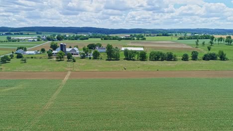 Eine-Luftaufnahme-Der-Farmlandschaft-Mit-Bepflanzten-Feldern-Und-Weiden,-Einem-Arbeitenden-Bauern-Und-Einem-Vorbeifahrenden-Zug-An-Einem-Schönen-Sonnigen-Tag