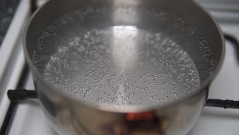 Close-up-of-water-bubbles-starting-to-form-before-boiling-in-a-stainless-steel-pot-on-the-fire-stove